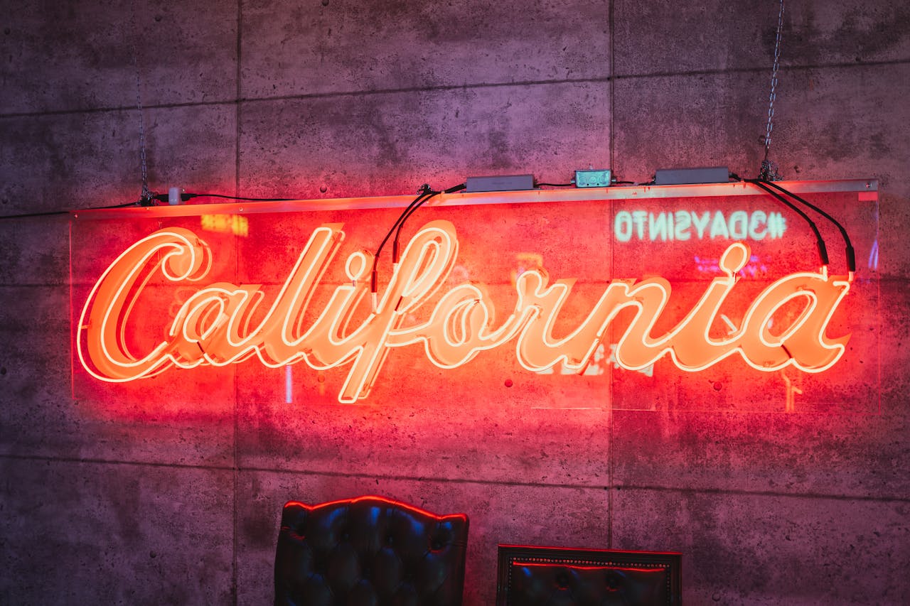 Bright neon sign with 'California' text glowing in a moody indoor setting.