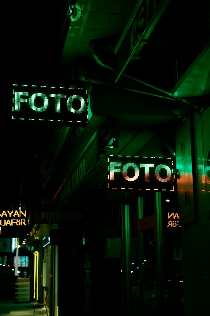 Illuminated city street with neon 'FOTO' signs at night.